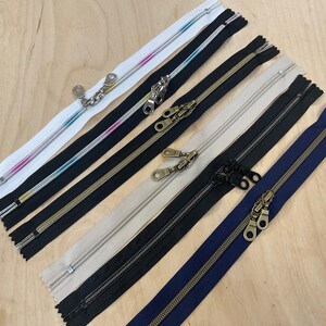 Puede incluir: Surtido de seis cintas de cremallera de diferentes colores, incluyendo blanco, rosa, azul, negro, beige y azul marino. Las cremalleras tienen tiradores de latón.