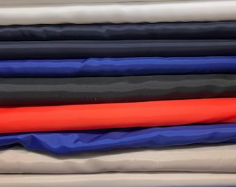 May include: A stack of colorful fabric rolls in various shades. The colors include white, navy, royal blue, black, red, and a light gray. The fabric appears to be a smooth, possibly synthetic material.
