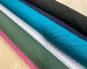 May include: Assortment of fabric rolls in various colors, including pink, green, white, teal, navy, and black. The fabric appears to be a lightweight material, possibly suitable for apparel or craft projects. The rolls are neatly arranged.