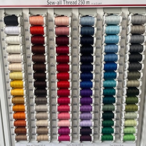 Puede incluir: Una pared con una muestra de carretes de hilo de colores, organizados por color. Los carretes están etiquetados con números y el texto "Sew-all Thread 250 m".