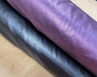 Pode incluir: Close-up de dois rolos de tecido de couro sintético. Um rolo é roxo profundo e brilhante, e o outro é azul escuro e suave. O tecido tem uma textura e brilho sutis, sugerindo um material de alta qualidade adequado para vários projetos.