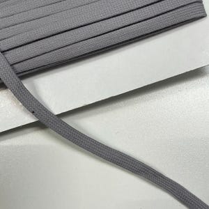 Könnte beinhalten: Nahaufnahme einer Rolle grauer Schnürsenkel. Die Schnürsenkel haben ein flaches, geflochtenes Design und sind einfarbig und neutral. Das Bild zeigt die Textur und Konstruktion der Schnürsenkel, die aus einem strapazierfähigen Material zu bestehen scheinen.