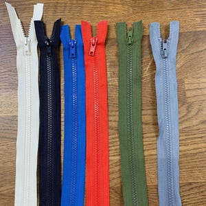 May include: A selection of six open zippers in a range of colours. The zippers are cream, black, blue, red, olive green, and grey. Each zipper shows the teeth and pull tab.