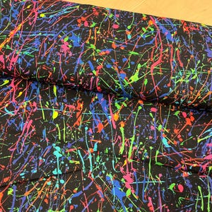 以下が含まれることがあります： 黒色の生地に、ネオンカラーのペイントスプラッターデザイン。ピンク、青、緑、オレンジ、黄色のスプラッシュが特徴で、大胆で芸術的なパターンを作り出しています。様々なクラフトやソーイングプロジェクトに最適です。