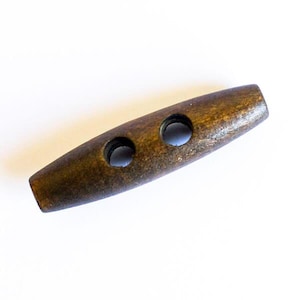 Könnte beinhalten: Ein dunkelbrauner Holz-Toggle-Knopf mit zwei Löchern. Der Knopf ist oval geformt und hat eine glatte Oberfläche.
