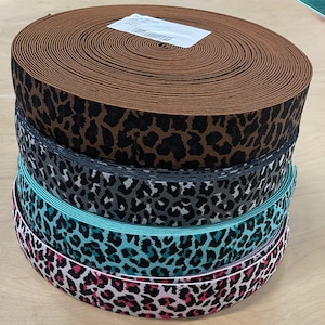 Puede incluir: Cuatro carretes de tejido elástico con estampado de leopardo. Los carretes están apilados uno encima del otro. El carrete superior es marrón, el segundo es gris, el tercero es turquesa y el inferior es rosa.