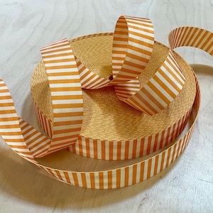 May include: A roll of orange and white striped ribbon. The ribbon is woven and has a textured surface.