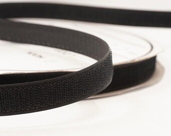 May include: Close-up of a roll of black hook and loop tape, also known as Velcro. The tape is a dark black color and has a textured surface. The roll is partially unraveled, showing the tape's construction.