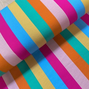 May include: A bolt of fabric featuring a repeating pattern of vertical stripes in vibrant colors including bright pink, light pink, orange, yellow, teal, and sky blue. The material is folded over itself, displaying the consistent striped design.