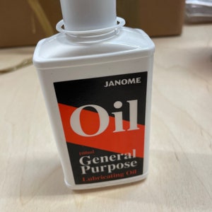May include: A white plastic bottle of Janome general purpose lubricating oil. The label features the word "Oil" in large, red letters against a black background. The bottle contains 100ml of oil.