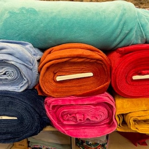 Könnte beinhalten: Ein Stapel Stoffrollen in verschiedenen Farben, darunter Blau, Orange, Rot, Pink und Gelb. Der Stoff ist weich und plüschig und perfekt für Bastel- oder Nähprojekte.