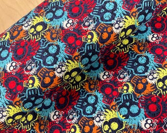 May include: A fabric with a repeating pattern of colorful skulls in red, yellow, orange, blue, and white against a dark blue background. The skulls have a distressed, graffiti-like appearance, creating a bold and edgy design.