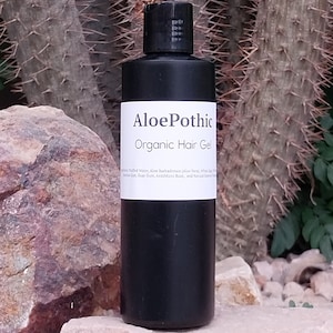 May include: A black bottle of "AloePothic Organic Hair Gel" with a white label, set against a backdrop of a cactus and rocks. The label lists ingredients. The bottle is cylindrical and has a black cap.