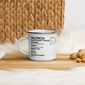 Puede incluir: Taza de esmalte blanco con un gráfico en blanco y negro de información sobre Valencia, Venezuela. El gráfico incluye las coordenadas de la ciudad, la fecha de fundación, la superficie total, la elevación y la temperatura promedio.