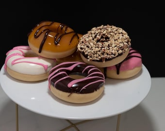 May include: A white plate with six assorted donuts. The donuts are topped with chocolate, sprinkles, and pink frosting.