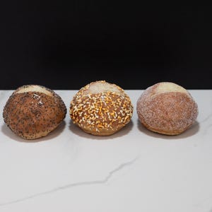 May include: Three round bread rolls with different toppings. The first roll is covered in poppy seeds, the second roll is covered in sesame seeds and the third roll is covered in sugar.
