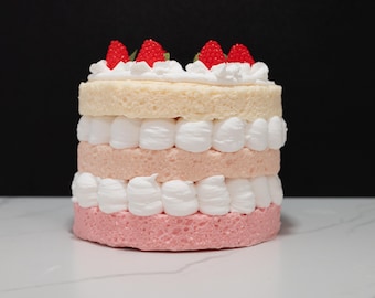 May include: A multi-layered cake with pink and white frosting and red strawberry decorations.