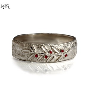 May include: A silver band ring with a textured surface and a design of a branch with red gemstones.