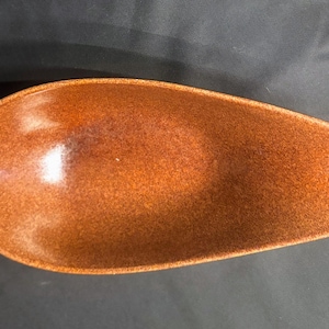 May include: A brown ceramic serving dish with a speckled finish. The dish is shaped like a long oval and has a slight curve.