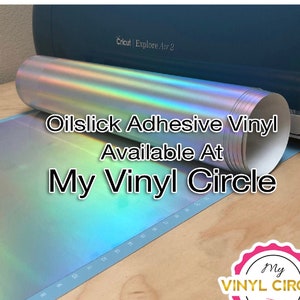 May include: A roll of iridescent oil slick adhesive vinyl on a cutting mat with a Cricut Explore Air 2 machine in the background. The text "Oilslick Adhesive Vinyl Available At My Vinyl Circle" is displayed on the image. A pink and white sticker with the text "My Vinyl Circle" is in the lower right corner.