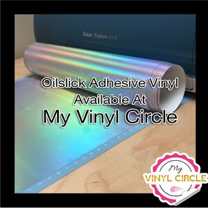 May include: A roll of iridescent oilslick adhesive vinyl, available at My Vinyl Circle. The vinyl is rolled up and sitting on a blue cutting mat with a Cricut Explore Air 2 machine in the background.