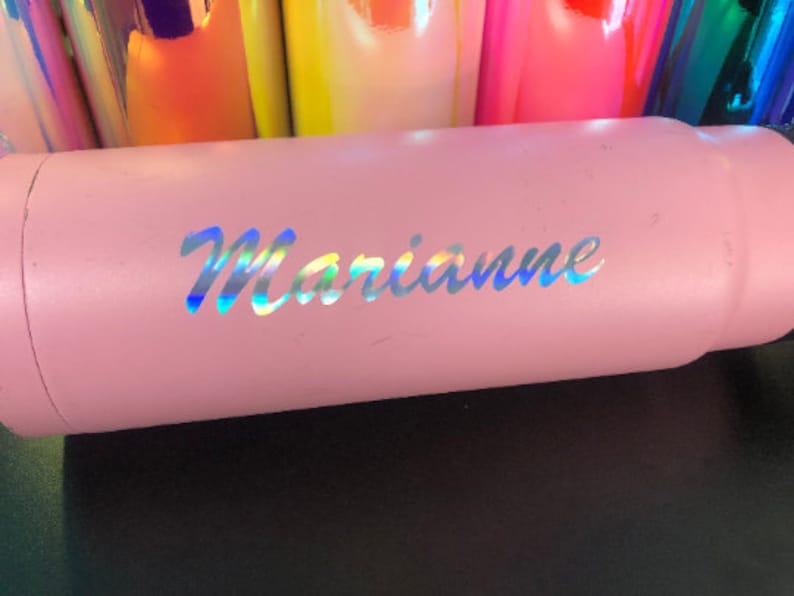 Puede incluir: Un vaso de acero inoxidable rosa con el nombre "Marianne" en letras iridiscentes.
