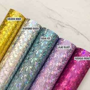 May include: Five rolls of iridescent vinyl with holographic glitter in different colors. The colors are gold, silver, blue, purple, and pink. The rolls are labeled "Golden Hour", "Diamond Disco", "Aqua Ice", "Lilac Blast", and "Fuchsia Frenzy".