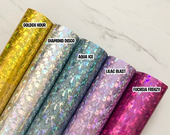 May include: Five rolls of iridescent vinyl with holographic glitter in different colors. The colors are gold, silver, blue, purple, and pink. The rolls are labeled "Golden Hour", "Diamond Disco", "Aqua Ice", "Lilac Blast", and "Fuchsia Frenzy".