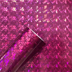 May include: A roll of iridescent pink vinyl with a holographic finish. The vinyl has a textured surface with a pattern of small, diamond-shaped pieces.