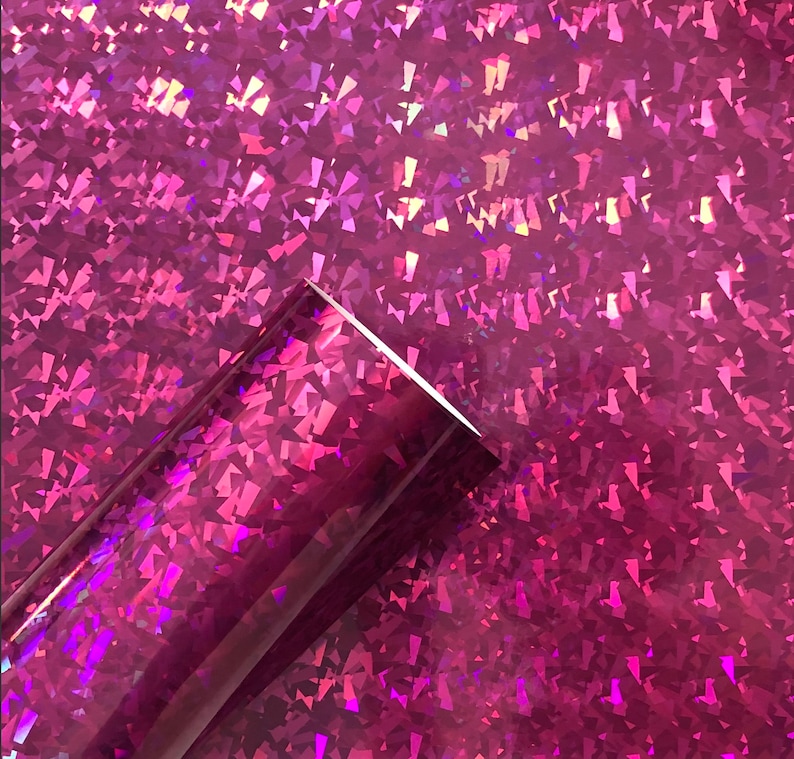 May include: A roll of iridescent pink vinyl with a holographic finish. The vinyl has a textured surface with a pattern of small, diamond-shaped pieces.
