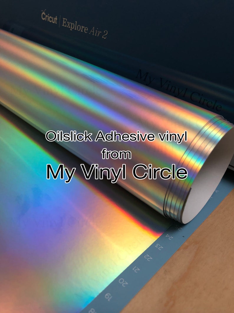 May include: A roll of iridescent oil slick adhesive vinyl from My Vinyl Circle. The vinyl is silver with a rainbow sheen. The text "My Vinyl Circle" and "Oilslick Adhesive vinyl from My Vinyl Circle" is printed on the roll.