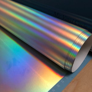 Puede incluir: Un rollo de vinilo hologr&aacute;fico iridiscente con una base de color plateado. El vinilo est&aacute; enrollado y tiene un n&uacute;cleo blanco. El vinilo est&aacute; etiquetado como "My Vinyl Circle".