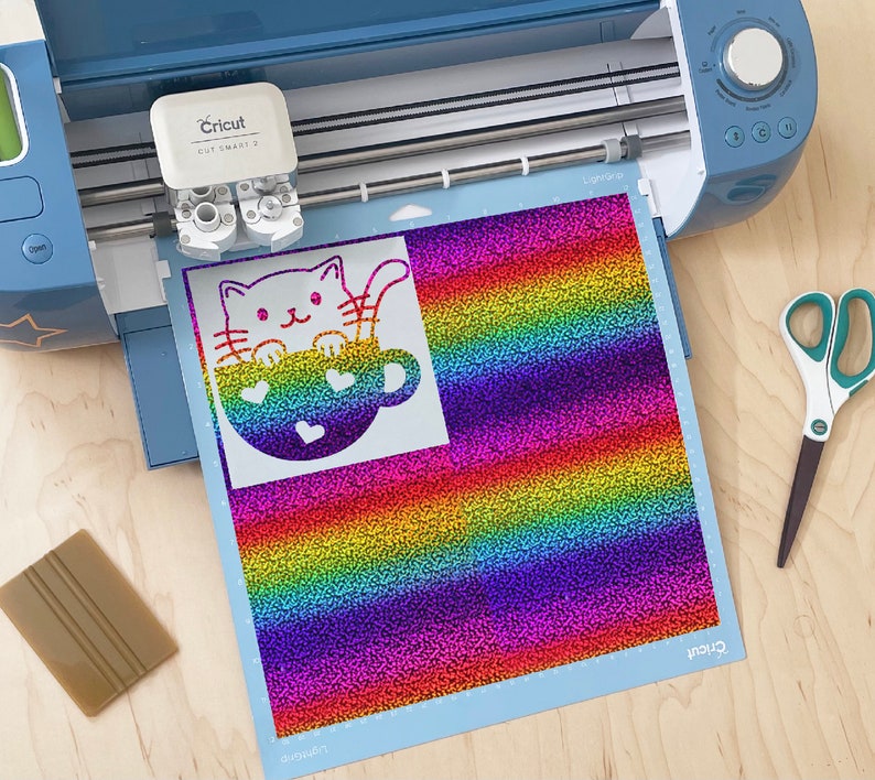 May include: A Cricut cutting machine with a rainbow glitter vinyl sheet featuring a white silhouette of a cat in a mug. The cat has a cute face and the mug has hearts on it.
