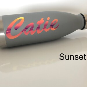 Peut inclure: Bouteille d'eau en acier inoxydable grise avec un autocollant en vinyle couleur coucher de soleil qui dit "Catie".