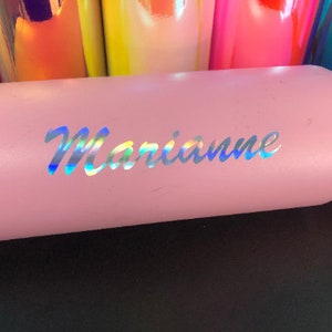 K&ouml;nnte beinhalten: Ein rosa isolierter Becher mit dem Namen "Marianne" in schillernden Buchstaben. Der Becher ist zylindrisch und scheint aus Metall zu sein. Im Hintergrund sind weitere bunte Becher zu sehen.