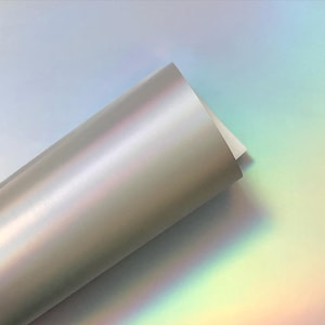 May include: A roll of iridescent silver vinyl with a holographic finish. The vinyl is rolled up and the end is slightly unfurled, revealing the iridescent surface.