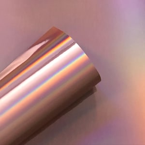 May include: A roll of iridescent rose gold vinyl with a holographic finish. The vinyl has a smooth, glossy surface and reflects light in a rainbow of colors.