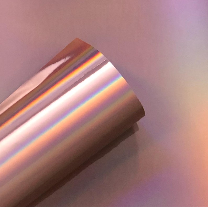 May include: A roll of iridescent rose gold vinyl with a holographic finish. The vinyl has a smooth, glossy surface and reflects light in a rainbow of colors.