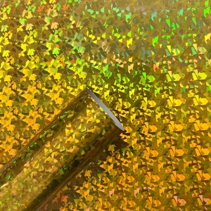 May include: A roll of iridescent gold holographic vinyl with a textured, geometric pattern. The vinyl is shiny and reflective.