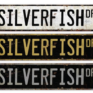 Può includere: Tre cartelli in metallo in stile vintage con il testo "SILVERFISH DR" in lettere nere, dorate e argentate su uno sfondo nero, bianco e nero, rispettivamente.