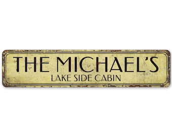 May include: Rustic metal sign with a yellowed background and black text that reads "The Michael's Lake Side Cabin".