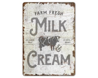 May include: White metal sign with distressed paint and black text that reads "Farm Fresh Milk & Cream". A black and white illustration of a cow is in the center of the sign. The text "Delivered Daily" is on the left side of the sign and "5 cents/quart" is on the right side.