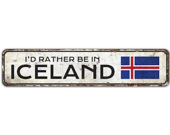 May include: A white metal sign with a distressed look, featuring the text "I'd rather be in ICELAND" in black lettering. The Icelandic flag is displayed on the right side of the sign.