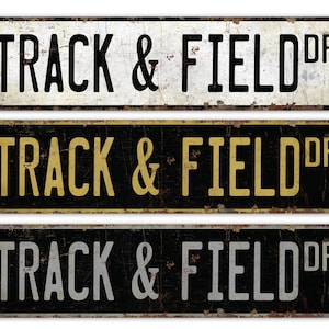 May include: Three vintage-style metal signs with the text "TRACK & FIELD DR" in black lettering on a white, black with gold, and black with silver background.