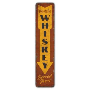 May include: A vintage-style metal sign with a distressed brown background and a yellow arrow pointing down. The arrow has the word "WHISKEY" written vertically in black letters. The sign reads "PREMIUM" at the top and "Served Here" at the bottom.