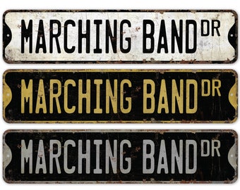 May include: Three vintage-style metal signs with the text "Marching Band Dr." in black, gold, and silver lettering on a black, white, and black background, respectively.