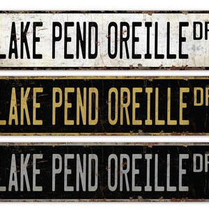 May include: Three vintage-style metal signs with the text "LAKE PEND OREILLE DR". The signs are rectangular with rounded corners and a distressed finish. The top sign is white with black text, the middle is black with yellow text, and the bottom is black with white text.