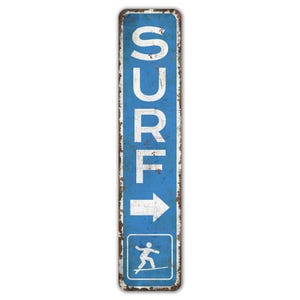 May include: A blue and white vintage-style metal sign with the word "SURF" in white letters and an arrow pointing to the right. The sign also features a white silhouette of a person surfing.