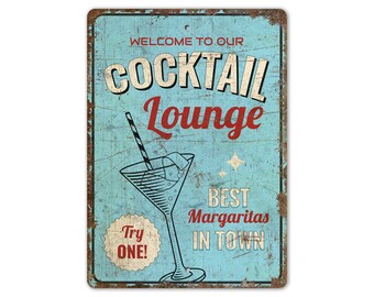Op de afbeelding: Een vintage metalen bord met een blauwe achtergrond en witte en rode tekst die "Welkom in onze cocktailbar De beste margarita's in de stad" zegt. Het bord heeft ook een martini-glas met een rietje en de tekst "Probeer er een!" in een cirkel.