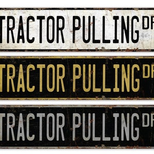 May include: Three vintage-style metal signs with the text "TRACTOR PULLING DR" in black, yellow, and gray lettering on a black, white, and black background.